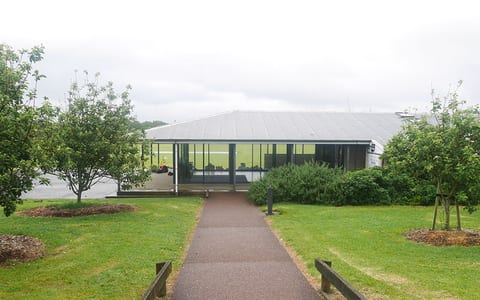 Low pavilion building beside cricket ground with pathway and trees