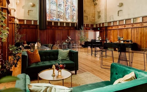 Church hall interior with dark timber panelling, stained-glass windows, and velvet sofas