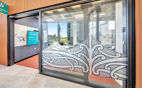 Glass entrance doors with decorative Māori-patterned etching on copper-clad building