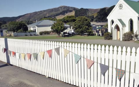 Small white timber chapel with green roof and arched entry, beside a white picket fence with bunting