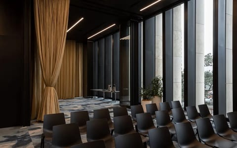 Dark-toned meeting room with floor-to-ceiling windows, city views, rows of dark chairs and gold drape partition