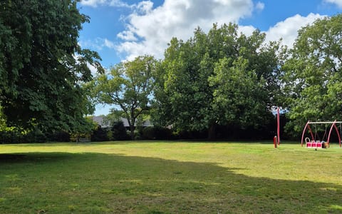 Open grass lawn with playground equipment and mature trees