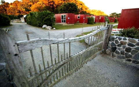 Rustic wooden entrance gate onto a gravel driveway with red cabin buildings beyond at dusk
