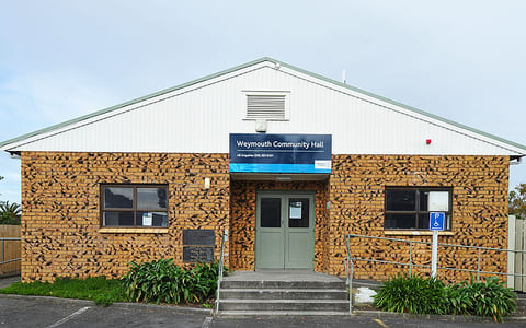 Tan brick hall with gabled white fascia, double green doors, and car park entry