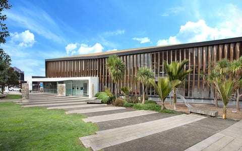 Low-rise contemporary building with horizontal timber louvre cladding, glass entry, and paved approach with planted borders