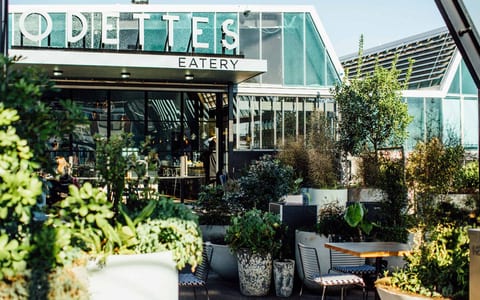 Rooftop eatery exterior with glass greenhouse addition, lush planted terrace and seating, black steel frame