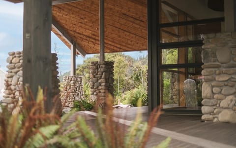 Stone and timber covered entry with stacked-stone columns, timber ceiling, and native planting