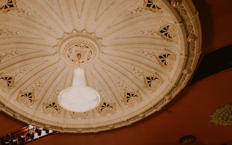 Ornate cream domed ceiling with gold detailing and a central pendant light fixture, terracotta walls