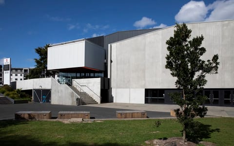 Large concrete and metal events building with external steps and timber seating, open grounds