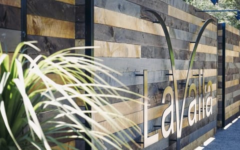 Horizontal timber-clad fence with a metal venue sign, green foliage in the foreground