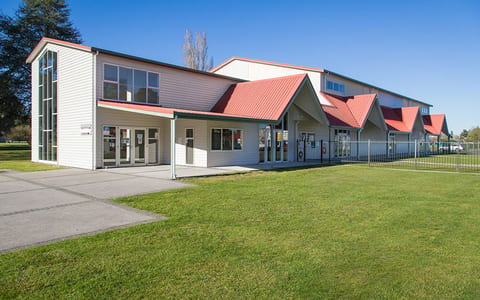 Long low building with white weatherboard cladding and red metal roof, set on a large lawn