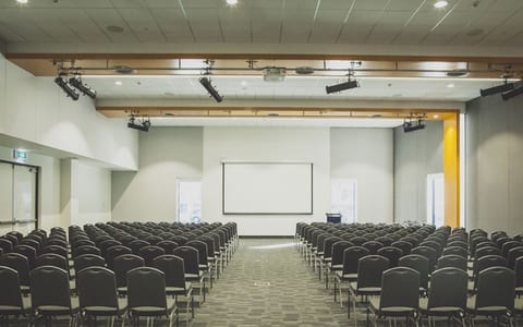 Large conference hall with rows of chairs and projection screen at front