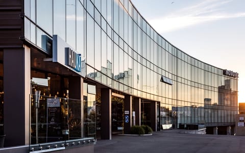 Curved glass-facade building exterior with dark columns and signage at sunset