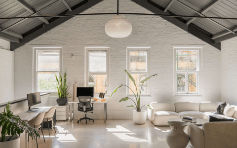White-painted brick interior with vaulted steel-truss roof, lounge seating, desks, and tall plants