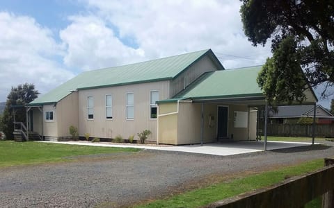 Single-storey metal-clad hall with green corrugated roof, covered entry, gravel forecourt