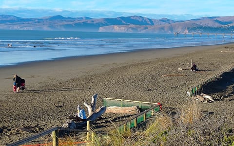 Sandy beach with hills in the background and people walking along the shore
