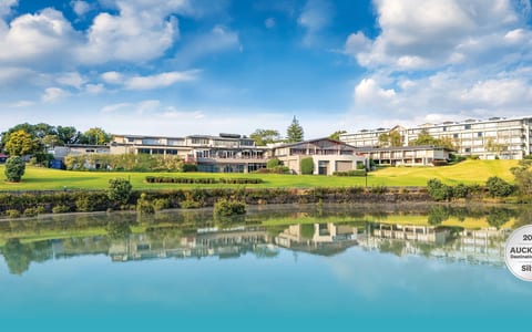 Multi-storey hotel complex reflected in still lake, surrounded by lawns and trees