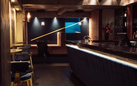 Dark intimate bar with navy velvet stools, lit bar counter, and pink booth seating