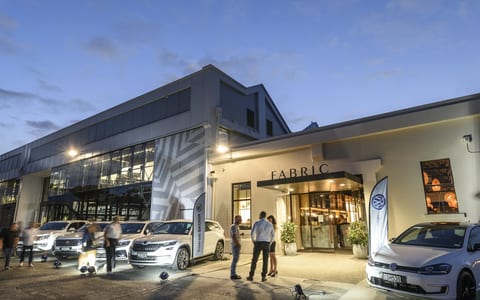White rendered commercial building exterior at dusk with illuminated entrance and vehicles outside