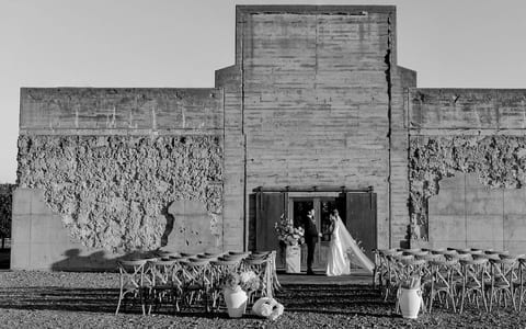 Rough concrete block building with stepped facade, rows of chairs set for outdoor ceremony