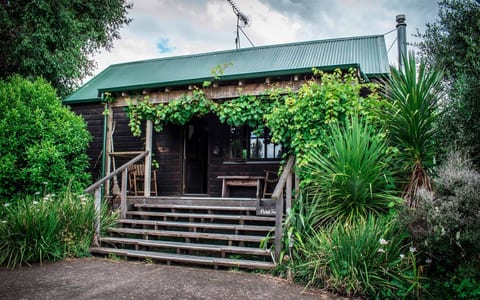 Dark timber cottage with covered verandah surrounded by lush garden