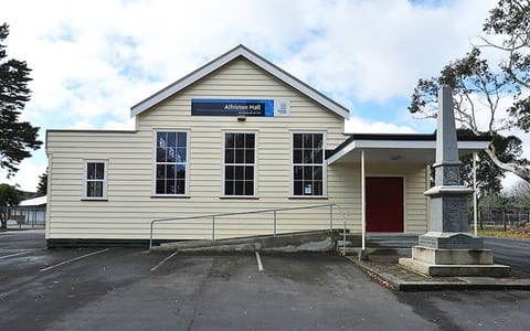 Cream weatherboard hall with red door and war memorial beside car park