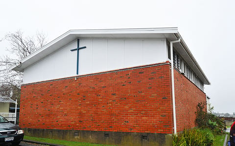 Brick hall exterior with cross mounted on white upper gable