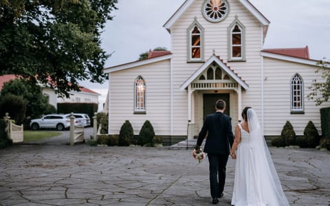 White timber church with gothic arched windows and red roof on paved forecourt