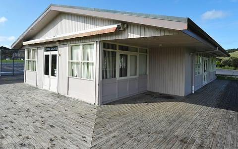 Single-storey weatherboard lounge building with deck on grass sports ground