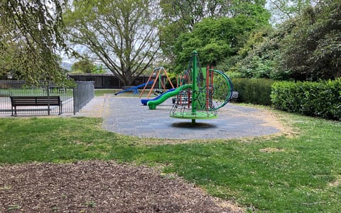Park lawn with playground equipment and mature trees