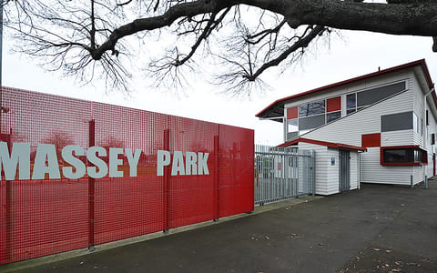 Park grandstand exterior with red signage fence and two-storey white weatherboard building