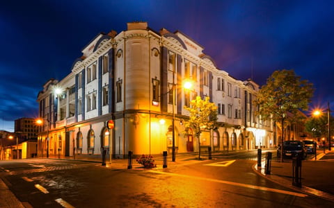 White heritage corner building with arched windows and ornate parapet, lit at night