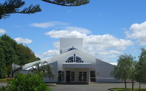 White modern church building with large arched entrance and surrounding trees