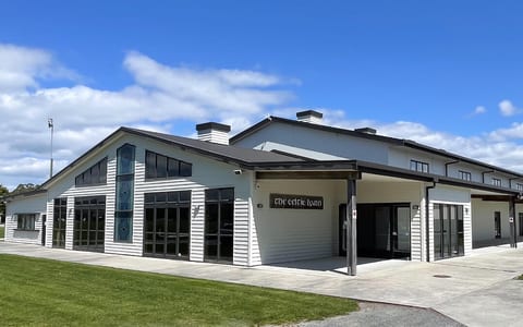 Large white and dark-trim barn building with stained-glass entry panels, open lawn