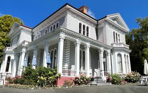 White two-storey Victorian villa with ornate columns, bay windows, and flowering garden beds