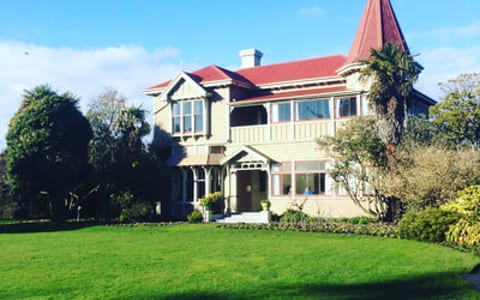 Two-storey heritage villa with red-roofed tower, set in a lawn with established trees