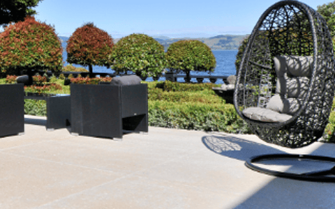 Stone-tiled terrace with suspended egg chair, dark cube seating, and lake and hills view under blue sky
