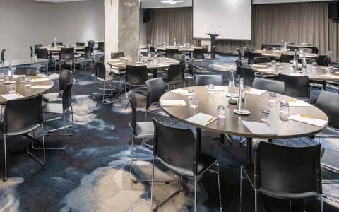 Hotel conference room with round tables, chairs, projector screen, and patterned carpet
