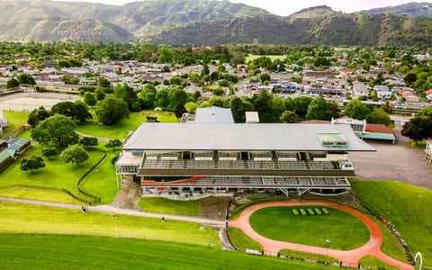 Aerial view of multi-level grandstand building at racecourse with green lawns and hills beyond