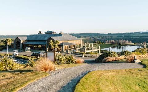 Rural resort building with metal roof beside a pond, viewed from a gravel driveway