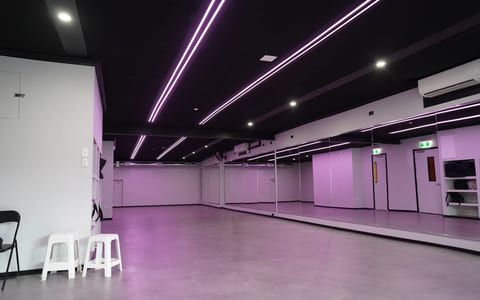 Bare concrete-floored studio with black ceiling, strip LED lighting, and a mirrored wall