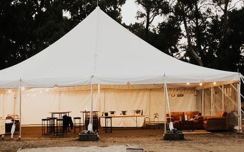 White marquee tent set up on farm grounds at dusk with festoon lights