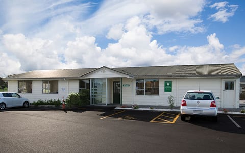 Single-storey white weatherboard community house with car park in foreground