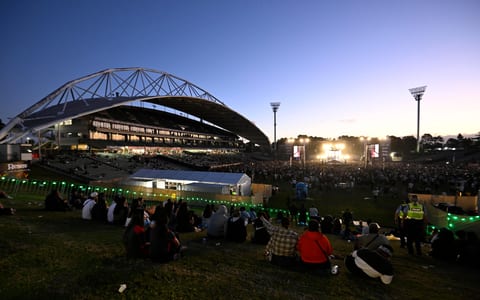Stadium exterior at dusk with large crowd and concert stage inside