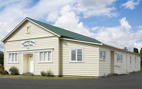 Cream weatherboard hall with green metal roof, gabled entry, and car park frontage