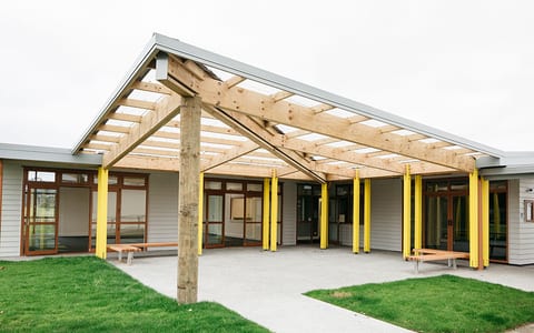 Modern single-storey community hub with timber pergola and yellow-painted columns