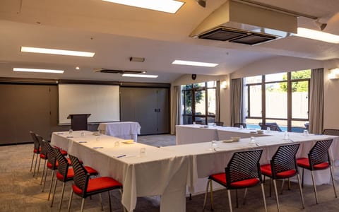 Plain conference room with white tables in U-shape layout, red-seated chairs, and projection screen