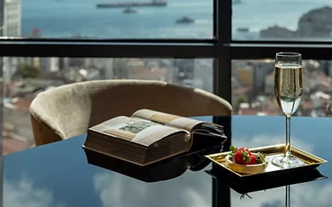 Glossy dark table with champagne glass, book, and small dish beside a panoramic city view