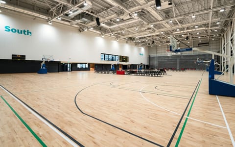 Large indoor sports hall with timber court markings, high ceiling, roof trusses and retractable seating