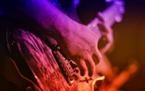 Close-up of hands playing electric guitar under coloured stage lighting